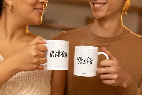 Smiling adult Brother and Sister standing side by side holding white mugs with the words Meisie and Bhudhi on them.